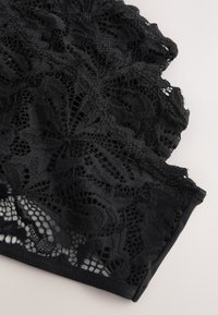 Tissu en dentelle noire avec motifs floraux et bords festonnés sur une surface claire, mettant en valeur la texture et un travail délicat.