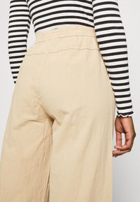 Pantalons beige à jambes larges avec une finition texturée, dotés d'une taille élastique. Haut à rayures noir et blanc à manches longues avec des poignets volantés.