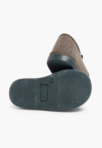 Hnědá texturovaná obuv na slip-on s kontrastní černou gumovou podrážkou; má malý obdélníkový prvek na podrážce pro zvýšení detailu.