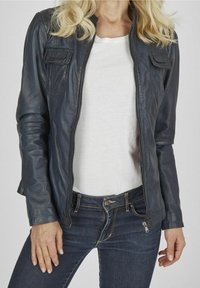 Námořnicky modrá kožená bunda se zapínáním na zip, dvěma kapsami na hrudi a přiléhavým střihem. Nošena přes bílou košili a v kombinaci s tmavými džínami.