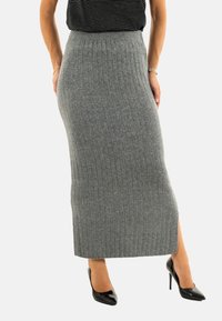 Falda de punto acanalado gris con cintura alta y abertura lateral, combinada con tacones altos de charol negros. Textura suave y silueta ajustada.
