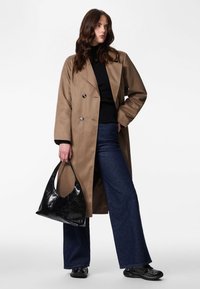 Brun trenchcoat med dobbeltradet knappelukking, kombinert med en svart turtleneck, mørke jeans og en svart skulderveske i lakk.