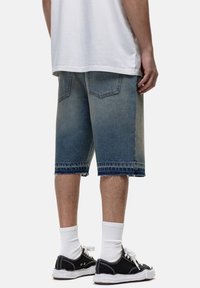 Bermuda jeans di colore blu chiaro con orlo sfrangiato, dotate di due tasche posteriori e un aspetto vissuto, abbinate a sneakers nere e calzini bianchi.