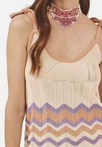 Top de punto en color crema con patrones en zigzag de melocotón, púrpura y marrón. Presenta tirantes anchos y un diseño de canalé texturizado. Acentuado con un collar de cuentas.
