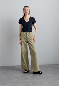 Black short-sleeve v-neck t-shirt paired with wide-leg olive green trousers and black slide sandals, set against a neutral background.