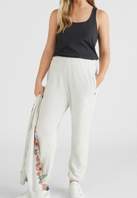 Pantaloni sportivi grigi con tasche laterali e dettagli floreali, abbinati a un top aderente nero. Sneakers bianche completano il look.