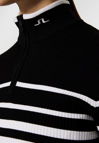 Svart ribbat långärmad topp med vita ränder, halvdragkedja och hög krage som har en liten logotyp på nacken.