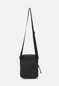 Sort crossbody taske lavet af slidstærkt stof, med firkantet form, justerbar rem og en frontlomme med lynlås og glat overflade.