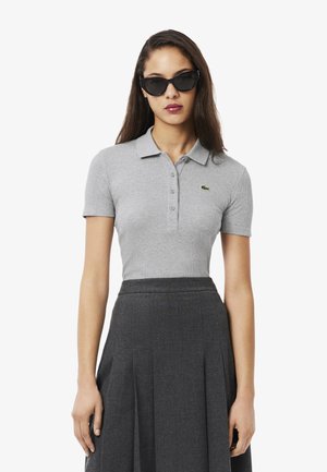 Grijze geribbelde polo met een drieknoopsluiting en een groen geborduurd logo, gecombineerd met een donkere geplooide rok voor een gestructureerd silhouet.
