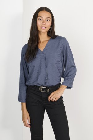 Blauw gestippeld blouse met een V-hals en een losse pasvorm, gecombineerd met zwarte skinny jeans en een riem met zilveren accenten. Flexibele textuur, lange mouwen.