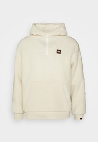 Cremefärgad fleece-hoodie med halvdragkedja framtill, framficka i kängurudesign, ribbad mudd och en logotyp-patch på v änster bröst.