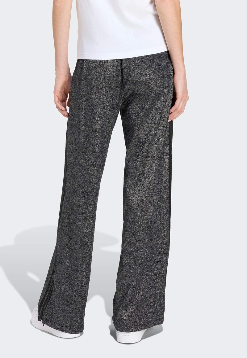 Pantalons de sport noirs étincelants avec une coupe évasée, présentant une texture lisse et des zips sur les côtés des ourlets pour une largeur ajustable.