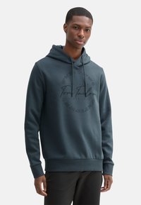 Felpa con cappuccio blu scuro con logo frontale che presenta delle coordinate, coulisse regolabile, polsini e orlo a coste. Tessuto morbido e testurizzato.