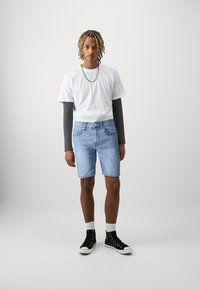 Denimshorts i lys blå, t-skjorte i hvit lagd med en mørk langermet skjorte, og svarte høy-top sneakers med hvite såler.