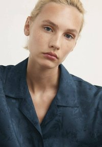 Mörkblå skjorta med blommönster, krage, mjuk textur och avslappnad passform. Tyget verkar vara lätt och andas.