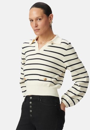 Maglione a righe in crema e blu navy. Presenta un colletto a polo e dettagli con bottoni dorati. Orlo a coste con un design aderente e maniche a palloncino.