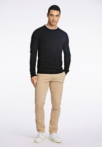 Maglione nero a girocollo, pantaloni chino beige e scarpe da ginnastica bianche. Il materiale sembra lavorato a maglia con polsini e orlo a coste. Design semplice e pulito.