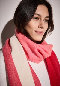 Écharpe douce et texturée aux teintes rose et rouge, avec une large bande crème, enroulée confortablement autour du cou.