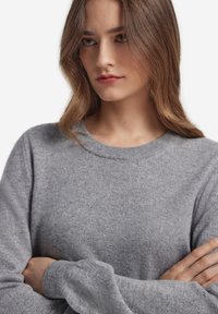 Szary sweter dziergany z okrągłym dekoltem i długimi rękawami. Miękka faktura, dopasowane rękawy oraz gładkie wykończenie.