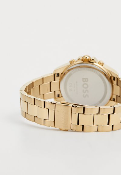 Montre en or avec un bracelet métallique, dotée d'un cadran rond, de boutons chronographes et d'un fermoir marqué "BOSS". Texture lisse et finition polie.
