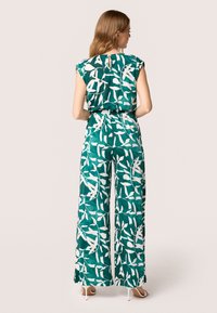 Groene jumpsuit met witte bladenpatronen, met kapmouwen, een ceintuur in de taille en een wijde pijpuitvoering. Soepele stoftextuur. Sleutelgatdetail op de rug.