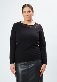 Schwarzer Pullover mit langen Ärmeln, Spitzenakzenten am Ausschnitt und subtilen funkelnden Details. Getragen mit einem schwarzen Lederrock.