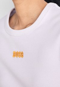 Ljuslila ribbad skjorta med rund halsringning och gult broderat "BOSS"-logotyp på framsidan. Slät textur.