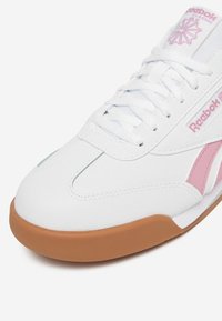 Scarpa sportiva bianca con accenti rosa, caratterizzata da una tomaia in pelle liscia, punta rotonda e suola in gomma naturale testurizzata.