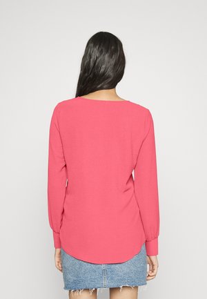 Maglia a maniche lunghe, di colore rosa, con scollo rotondo e orlo curvo, abbinata a una gonna di jeans. Tocco morbido, vestibilità casual.