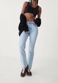 Jasnoniebieskie spodnie z wysokim stanem, czarny krótki top, oversize czarny kardigan i ciemnobrązowe sneakersy z kremowymi sznurówkami.