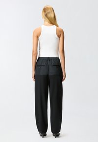 Pantaloni neri a vita alta con gamba affusolata, caratterizzati da una texture liscia, una cintura elastica e due tasche posteriori con cerniere.
