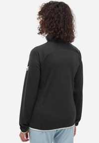 Veste zippée noire à manches longues, en tissu texturé et avec un col montant. Comprend des poches latérales et un détail de taille contrastant.