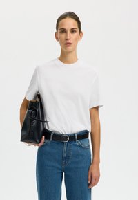 Witte katoenen t-shirt, ronde halslijn, gecombineerd met hooggesneden blauwe denim jeans en een zwarte leren handtas met een ronde handgreep.