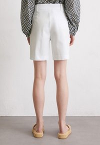 Pantaloni corti bianchi sartoriali con una vestibilità dritta, realizzati in tessuto liscio, con tasche posteriori e orlo pulito. Abbinati a sandali con piattaforma intrecciata.