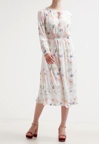 Vestido floral de manga larga con fondo blanco, cintura elástica, borde de encaje en los puños y el dobladillo, y detalles de volantes en la parte inferior.
