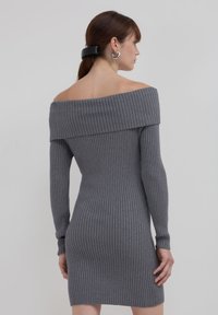 Grau geripptes Strickkleid mit schulterfreiem Design, langen Ärmeln und einer figurbetonten Silhouette, das subtile Texturen aufweist und eine Länge bis zur Mitte des Oberschenkels hat.
