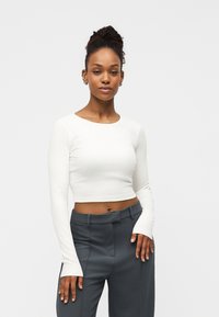 Λευκό ριμπ cropped μπλουζάκι με μακριά μανίκια, συνδυασμένο με ψηλόμεσο παντελόνι σε σκούρο γκρι. Διαθέτει απαλή υφή και εφαρμοστή γραμμή.