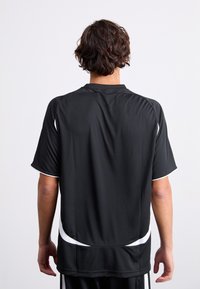 Musta lyhythihainen urheilupaita, jossa on tekstuurikuvio ja valkoiset tehosteet helmoissa ja sivuilla. Takakatselu esitetty.