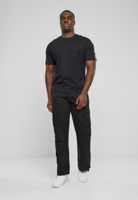 T-shirt en coton noir à manches courtes, associé à un pantalon cargo noir avec poches latérales. Des baskets blanches complètent la tenue.