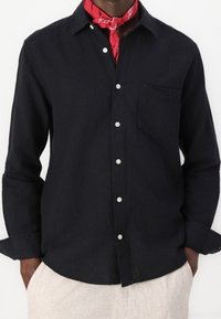 Sort langærmet skjorte med knappet krave, brystlomme og hvide knapper; kombineret med et rødt mønstret bandana.