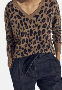Leopardmönstrad tröja i beige och brunt, med V-ringning och ribbade ärmslut. Bärs tillsammans med högmidjade mörk denimbyxor och knytning i midjan.