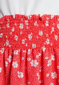 Red floral dress bodice features a smocked texture with small white flowers and a ruffled neckline, creating a fitted design above a flared skirt.