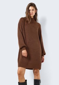 Brun strikket kjole med høy krave, lange ermer og ribbestrikket tekstur. Designet er oversized, og ender midt på låret, med tettsittende mansjetter.