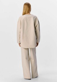 Beige oversized skjorte med faldne skuldre, rund halsudskæring og en glat tekstur, parret med matchende brede bukser.