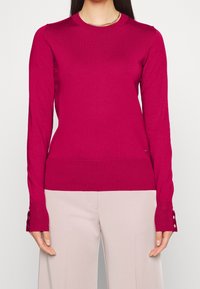 Fuchsia gebreide trui met lange mouwen en knoopmanchetten, voorzien van een ronde hals en geribde zoom, gemaakt van een gladde, rekbare stof.