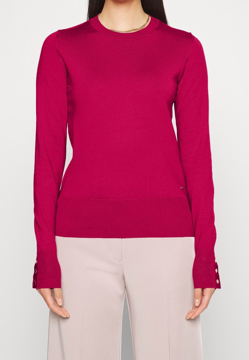 Fuchsia gebreide trui met lange mouwen en knoopmanchetten, voorzien van een ronde hals en geribde zoom, gemaakt van een gladde, rekbare stof.