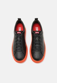 Baskets en cuir noir avec un bout rond, présentant un design perforé. Semelle en caoutchouc orange vif avec des lacets noirs et des semelles intérieures rouges.