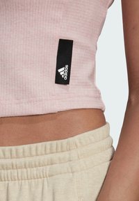 Růžový ribbed zkrácený top s černým štítkem Adidas, spárovaný se světle béžovými kalhotami s elastickým pasem. Zaměřte se na texturu látky a střih.