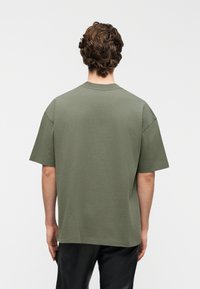 Χακί πράσινο βαμβακερό μπλουζάκι με χαλαρή εφαρμογή, κοντά μανίκια και στρογγυλή λαιμόκοψη, με απλή υφή και χωρίς ορατά σχέδια.