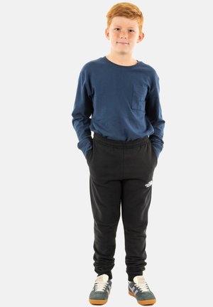 Camisa azul de manga larga con un bolsillo frontal, pantalones jogger negros y zapatillas grises con suelas naranjas. Diseño sencillo, ajuste casual.